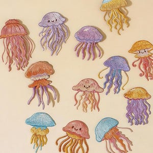 May include: Embroidered jellyfish patches in various colors, including pink, purple, blue, and yellow, with delicate thread details. The patches are arranged on a light beige background. The text "Longancraft" is at the top.