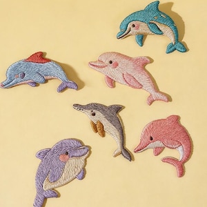 May include: Embroidered dolphin patches in various colors, including blue, pink, and purple. The patches feature detailed stitching and are arranged on a yellow background. The text "Longancraft" is at the top.