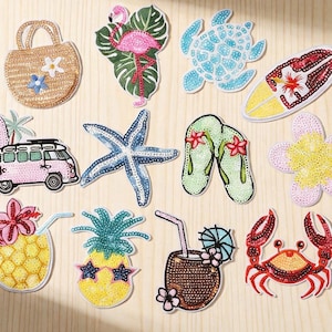 May include: A collection of twelve embroidered patches featuring summer themes including a straw bag, flamingo, sea turtle, surfboard, camper van, starfish, flip-flops, flower, pineapple drink, pineapple with sunglasses, coconut drink, and a red crab.
