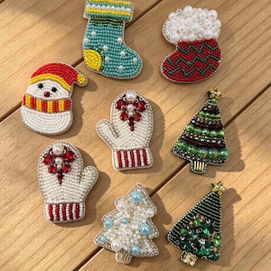 May include: A collection of eight holiday-themed beaded pins featuring two Christmas stockings, a snowman, two mittens, and three Christmas trees. Each pin is intricately crafted with colourful glass beads, pearls, and crystals. The text Longancraft is visible at the top.