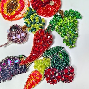 May include: A collection of beaded fruit and vegetable brooches, including a red apple, green grapes, and a red chili pepper. The brooches are made with colorful beads and sequins, and the text "Longancraft" is at the top.