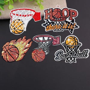 Op de afbeelding: Een verzameling patches met basketbalthema. De patches tonen basketballen, manden en de teksten "HOOP there it is!" en "Basketball". De patches zijn in rood, oranje en wit, sommige met een glittereffect.