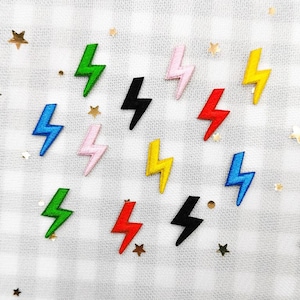 Puede incluir: Un conjunto de parches de rayos de colores, en verde, azul, rosa, amarillo, rojo y negro. Los parches están dispuestos sobre un fondo de tela blanca con pequeños detalles de estrellas y puntos dorados. El texto "Longancraft" se encuentra en la parte superior.