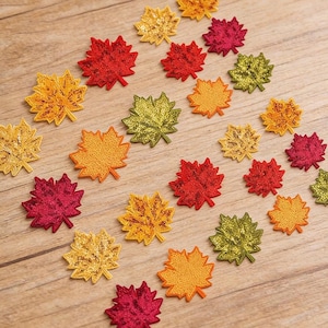 May include: Embroidered maple leaf appliques in various fall colors, including red, gold, orange, and green, scattered on a wooden surface. The text "Longancraft" is displayed at the top. These decorative leaves are ideal for crafting and seasonal projects.