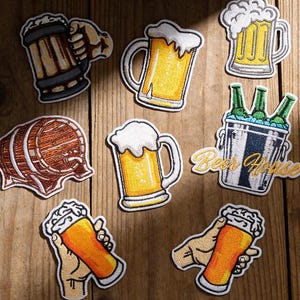 May include: A collection of eight embroidered patches featuring beer-themed designs, including mugs of beer with foam, a wooden barrel, and a metal bucket containing green beer bottles with the text Beer House embroidered in yellow thread.