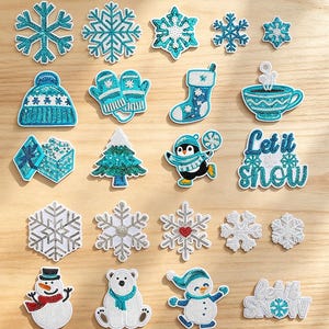 May include: A collection of embroidered patches featuring winter and holiday themes, including snowflakes, a beanie, mittens, a stocking, a mug, a gift, a tree, a penguin, a snowman, a polar bear, and text reading Let it snow in blue and white.