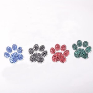 May include: Four paw print iron-on patches in blue, black, red, and green. Each patch is made of sequins.