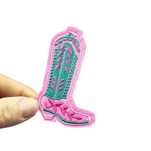 May include: A pink embroidered cowboy boot patch with green and pink floral detailing. The patch has the text "Longancraft" at the top. This patch is ideal for adding a touch of Western flair to clothing or accessories.