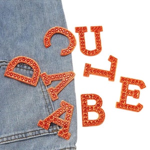 May include: Orange rhinestone letters spelling out the word "CUTE" on a blue denim background.