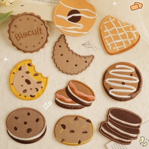 Peut inclure: Un ensemble de dix patchs brodés thermocollants représentant différents modèles de biscuits. Les patchs sont de couleur marron, jaune et blanc et présentent des motifs tels qu'un biscuit aux pépites de chocolat, un biscuit sablé et un biscuit sandwich.