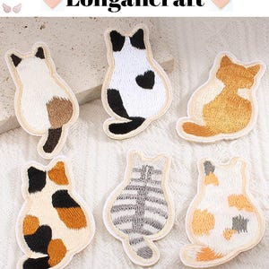 Peut inclure: Plusieurs écussons brodés en forme de chat, dans des tons de blanc, marron, noir et orange. Chaque écusson représente un chat vu de dos, avec des coutures détaillées et une bordure crème. Le texte "Longancraft" est visible en haut.