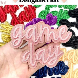Peut inclure: Écussons brodés avec l'inscription "Game Day" en script rose pailleté. D'autres écussons rouges, verts, violets, noirs, dorés et bleus sont également visibles. La marque "Longancraft" est en haut.