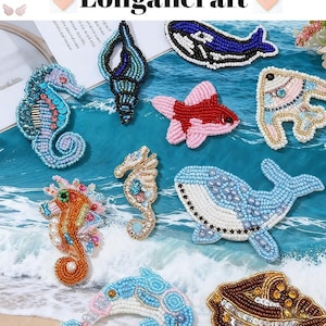 Peut inclure: Une collection d'épingles en forme de créatures marines perlées, comprenant des hippocampes, des baleines, des poissons et un coquillage. Les épingles sont de différentes couleurs, comme le bleu, l'orange, le rose et l'or. Le texte "Longancraft" est en haut.