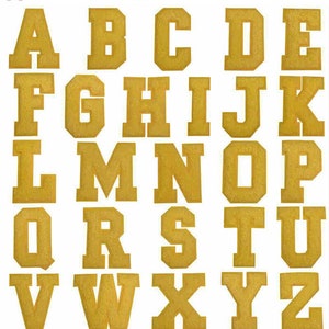 May include: A set of 26 gold felt iron-on letters, A through Z, in a varsity style font. The letters are arranged in three rows, with the first row being A through E, the second row being F through J, and the third row being L through Z. The letters are all the same size and are on a white background.