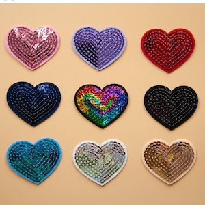 Peut inclure: Neuf patchs en forme de cœur avec des embellissements en paillettes de différentes couleurs, notamment rose, violet, rouge, bleu, arc-en-ciel, noir, turquoise, argent et or. Les patchs sont disposés en trois rangées de trois. Longancraft.