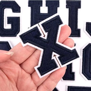 May include: A set of navy blue felt iron-on letters with white outlines. The letters are G, H, I, X, and L. The letters are in a varsity style font.
