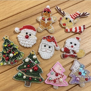 Può includere: Una collezione di nove toppe ricamate a tema natalizio, tra cui volti di Babbo Natale, figure di pan di zenzero, renne e alberi di Natale decorati in verde, rosa e viola, realizzati con perline, perle e paillettes.