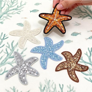 May include: A collection of sequined starfish patches in various colors, including gold, silver, blue, and brown. One patch is held by a hand. The patches are on a white background with a sea life design. The text "Longancraft" is at the top.