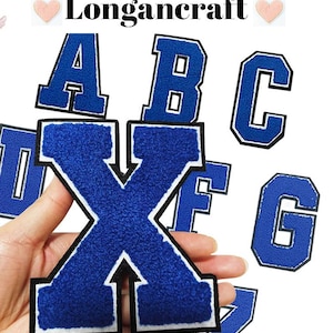 May include: A set of blue felt letter patches with white outlines. The letters are A, B, C, D, X, F, G, and Z. The letters are arranged in a random order. The letters are all uppercase.