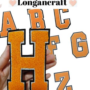 Może przedstawiać: Zestaw liter termotransferowych z filcu pomarańczowego, w tym A, B, C, F, G, H i Z. Litery mają biały kontur i czarne szwy.