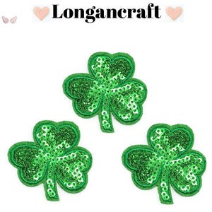 May include: Three green sequined shamrock patches with a dark green border are displayed on a white background. The text "Longancraft" is at the top of the image. The shamrocks are a symbol of St. Patrick's Day.