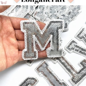 Peut inclure: Lettres en paillettes argentées avec un contour blanc. Les lettres sont M, I et G. Les lettres sont sur un fond blanc.