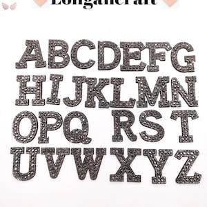May include: A set of 26 iron-on alphabet letters, each letter is covered in black rhinestones. The letters are uppercase and are arranged in alphabetical order.
