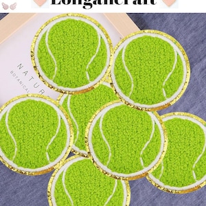 Może przedstawiać: Sześć zielono-białych naszywek w kształcie piłki tenisowej z złotą obwódką. Naszywki są wykonane z puszystej tkaniny i idealnie nadają się do dodania sportowego charakteru ubraniom lub akcesoriom.