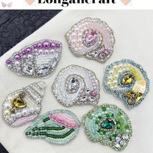 May include: Six different beaded and jeweled shell-shaped embellishments. The embellishments are in various colors, including pink, green, white, and yellow. They are all about 2 inches in diameter.