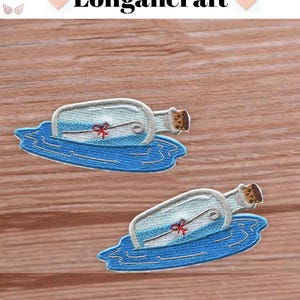 May include: Two embroidered patches with a message in a bottle design. The clear bottle has a cork, a red bow, and a scroll inside. The bottle floats on blue water. The text "Longancraft" is at the top.