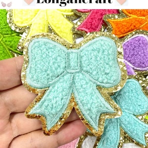 May include: A light blue fuzzy bow with gold glitter trim. The bow is surrounded by other bows in various colours.