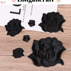 May include: Five black felt rose patches of varying sizes. The largest rose patch is about 10 cm wide. The patches are on a light brown wooden surface.