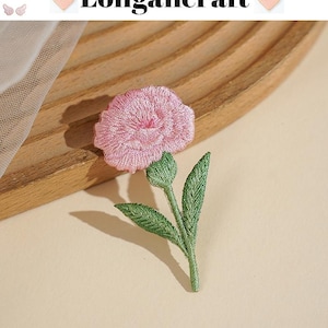 May include: Embroidered pink flower with green leaves and stem. The flower has a detailed, textured appearance. The image includes the text "Longancraft" at the top. The flower is likely a patch or applique for clothing or crafts.