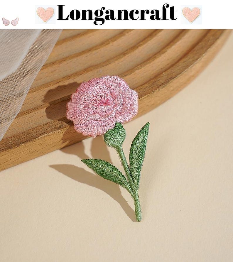 May include: Embroidered pink flower with green leaves and stem. The flower has a detailed, textured appearance. The image includes the text "Longancraft" at the top. The flower is likely a patch or applique for clothing or crafts.