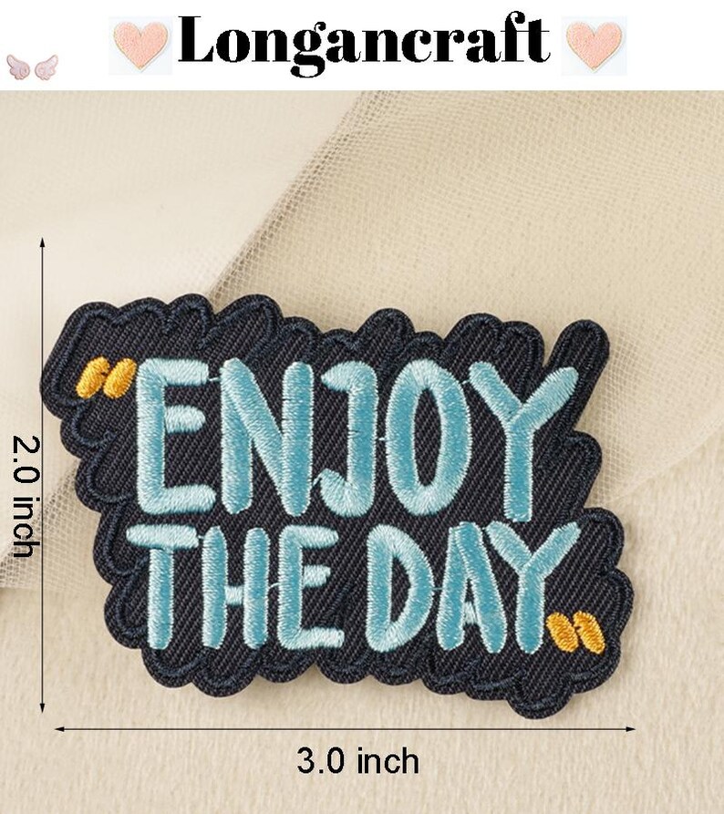Pode incluir: Um remendo de ferro bordado azul e preto com o texto "Enjoy the Day" em um contorno branco. O remendo mede 7,6 cm de largura e 5,1 cm de altura.
