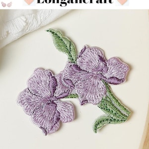 May include: Embroidered floral patches featuring two purple flowers with green leaves. The patches have a detailed stitch design and are set against a white background. The text "Longancraft" is at the top.