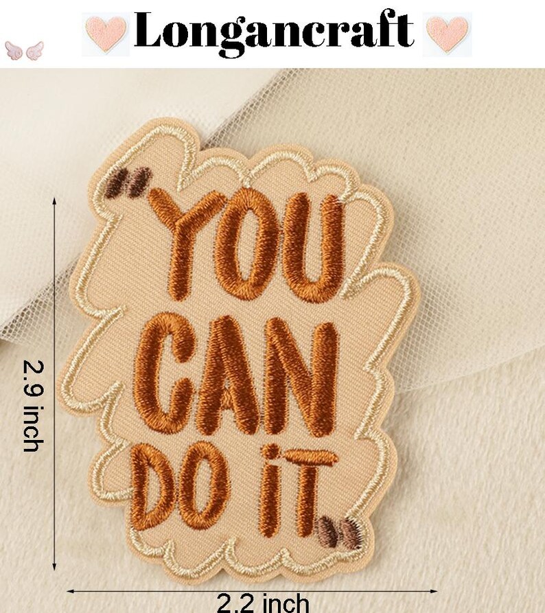 Pode incluir: Etiqueta bordada de ferro bege com o texto "You Can Do It" em fio marrom. A etiqueta mede 5,6 cm de largura e 7,4 cm de altura.