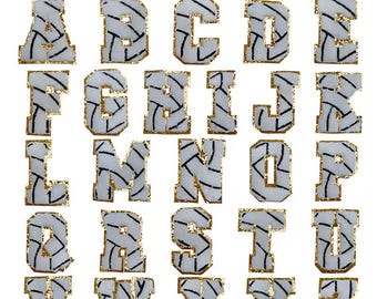 Può includere: Un alfabeto completo di lettere in tessuto, dalla A alla Z. Ogni lettera ha uno sfondo bianco con un motivo geometrico nero e bordi dorati. Il nome del marchio "Longancraft" è visibile in alto.