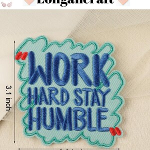 Pode incluir: Patch bordado azul com o texto "Work Hard Stay Humble" em forma de nuvem. O patch mede 3,1 polegadas de altura e 3 polegadas de largura.