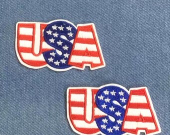 Può includere: Due toppe ricamate "USA" in rosso, bianco e blu. La "U" e la "A" presentano strisce rosse e bianche, mentre la "S" è blu con stelle bianche. Sono su uno sfondo di denim blu. Il marchio "Longancraft" è in alto.