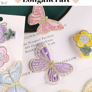 May include: Assortment of embroidered iron-on patches featuring butterflies and flowers. The butterflies are in pink, purple, and blue with gold glitter accents. The flowers are yellow and pink with green stems and gold glitter accents.