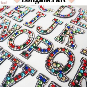May include: A set of colourful alphabet letters made of rhinestones. Each letter is outlined in black and has a variety of coloured rhinestones.