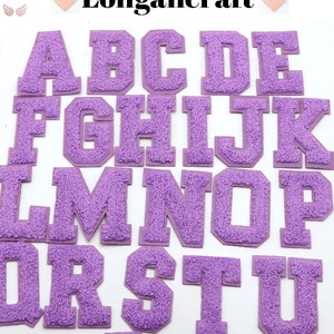May include: A collection of purple chenille letter patches in a collegiate style. The letters A through U are visible, with a fuzzy texture and a solid purple border. The brand name "Longancraft" is at the top.