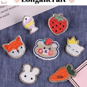 May include: A set of 8 embroidered iron-on patches featuring various designs, including a fox, a bear, a bunny, a fish, a strawberry, a carrot, and a cloud with a crown. The patches are all on a blue denim background.