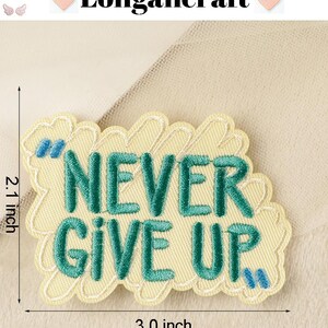 Pode incluir: Um remendo bordado amarelo com uma mensagem verde "NEVER GIVE UP". O remendo tem 7,6 cm de largura e 5,3 cm de altura.