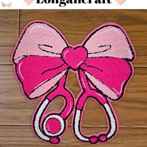 May include: Pink and white felt bow with a stethoscope in the centre. The bow has a heart shape in the centre. The background is a wooden surface.