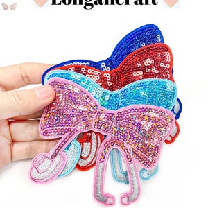 May include: Three sequined bow patches in pink, blue and red. The bows are layered on top of each other, with the pink bow on top. The bows have a sparkly finish and are perfect for adding a touch of sparkle to any project.