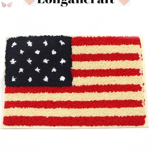 Puede incluir: Un parche de bandera estadounidense rojo, blanco y azul con una textura peluda. La bandera tiene 13 rayas y 50 estrellas blancas sobre un campo azul.