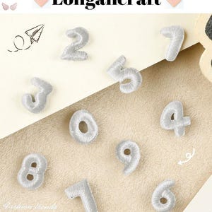 May include: Ten white felt iron-on patches with numbers 0 through 9. The patches are on a white surface.