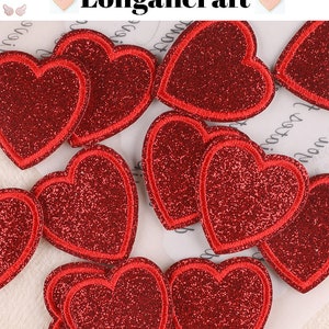 Puede incluir: Una colección de parches en forma de corazón rojo con purpurina y contorno rojo. Los parches están dispuestos sobre una superficie blanca.